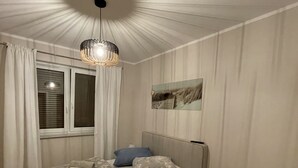 A bedroom with a bed, curtains, a window, a ceiling light fixture, and a wall-mounted artwork.