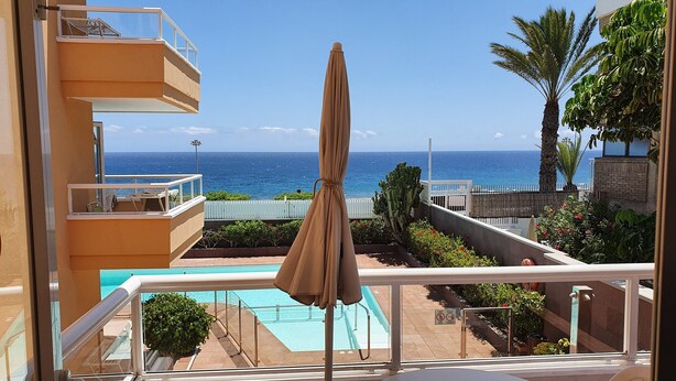 Un balcone con vista sull'oceano, una piscina e un ombrellone.