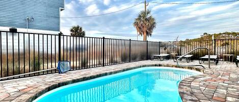Une piscine à bord incurvé, entourée d’une terrasse en briques et d’une clôture en métal.