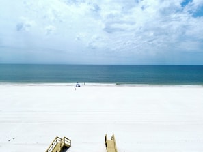 A beach with a wooden walkway leading to the water, a clear sky, and a calm sea.