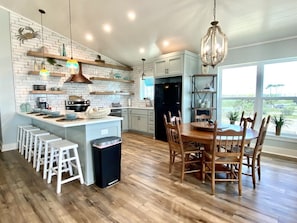 A modern kitchen with a central island, wooden stools, and a dining table with chairs.