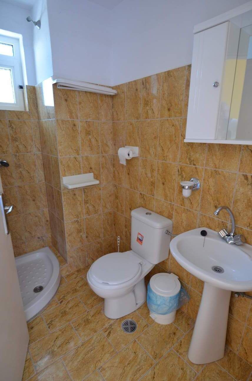 A bathroom with a toilet, bidet, and sink, all in white, with beige marble tiles on the walls.