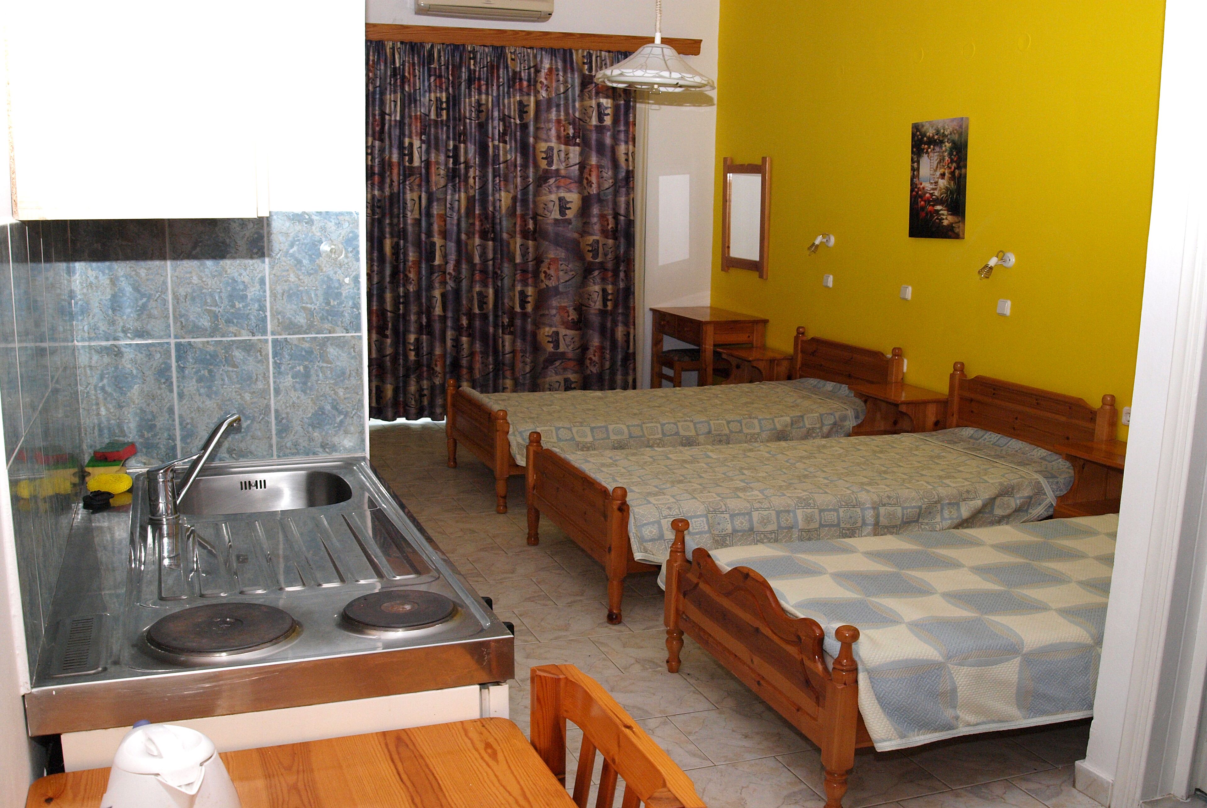 A compact room with a kitchen area, two wooden beds, a dining table, and a curtain with a pattern.