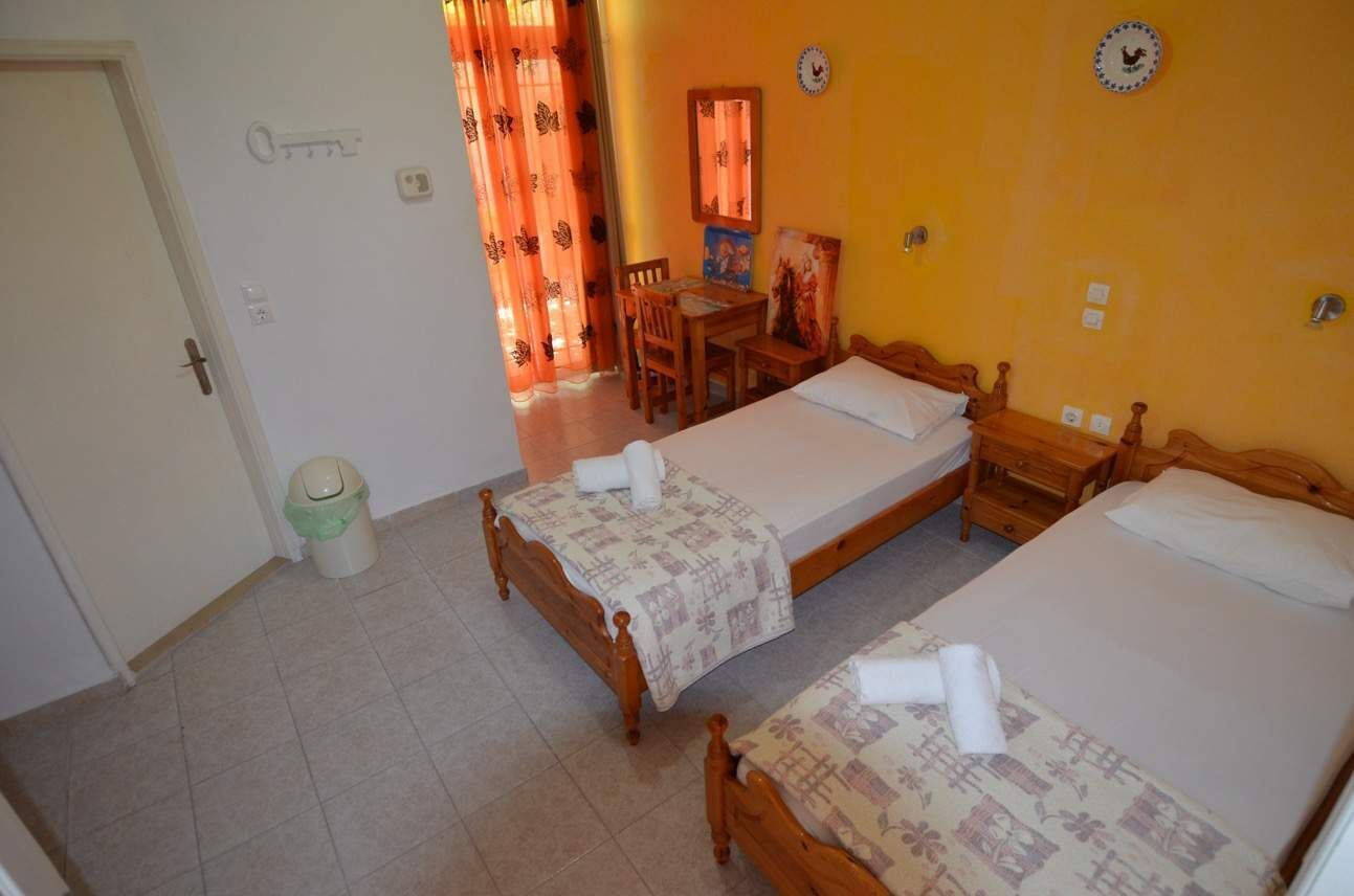 A room with two wooden beds, a small table, a chair, and a window with curtains.