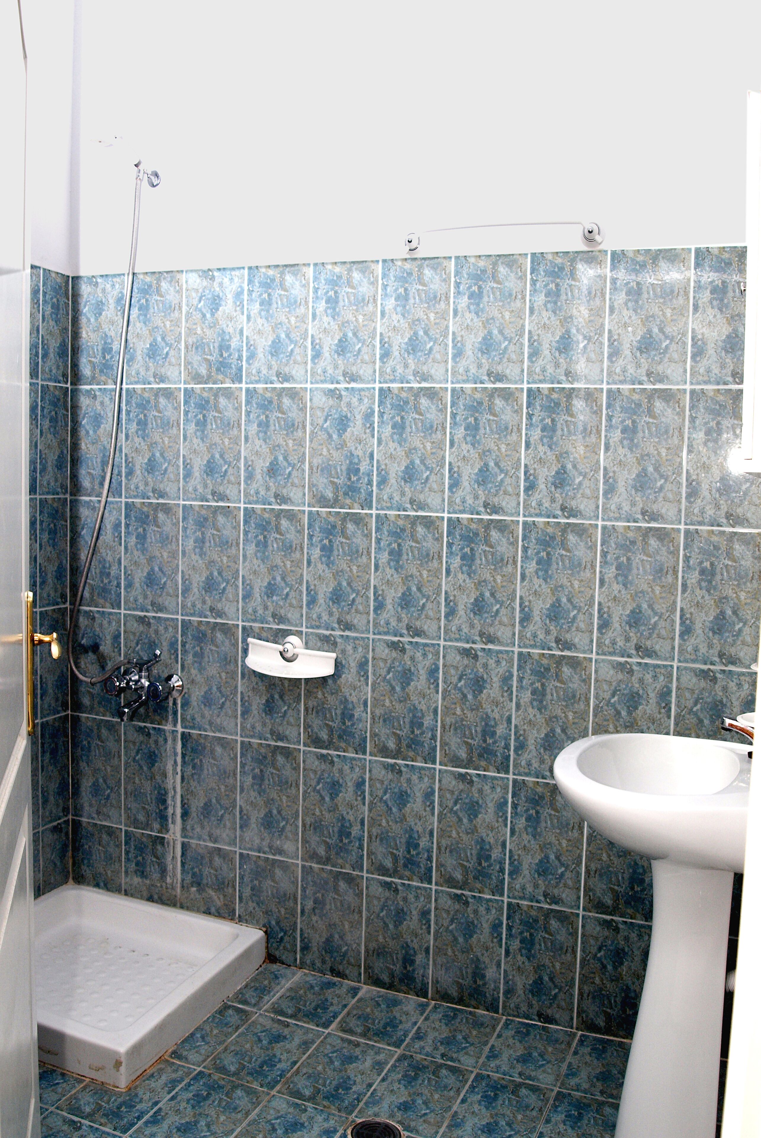 A bathroom with blue tiles, a shower, a toilet, and a sink.