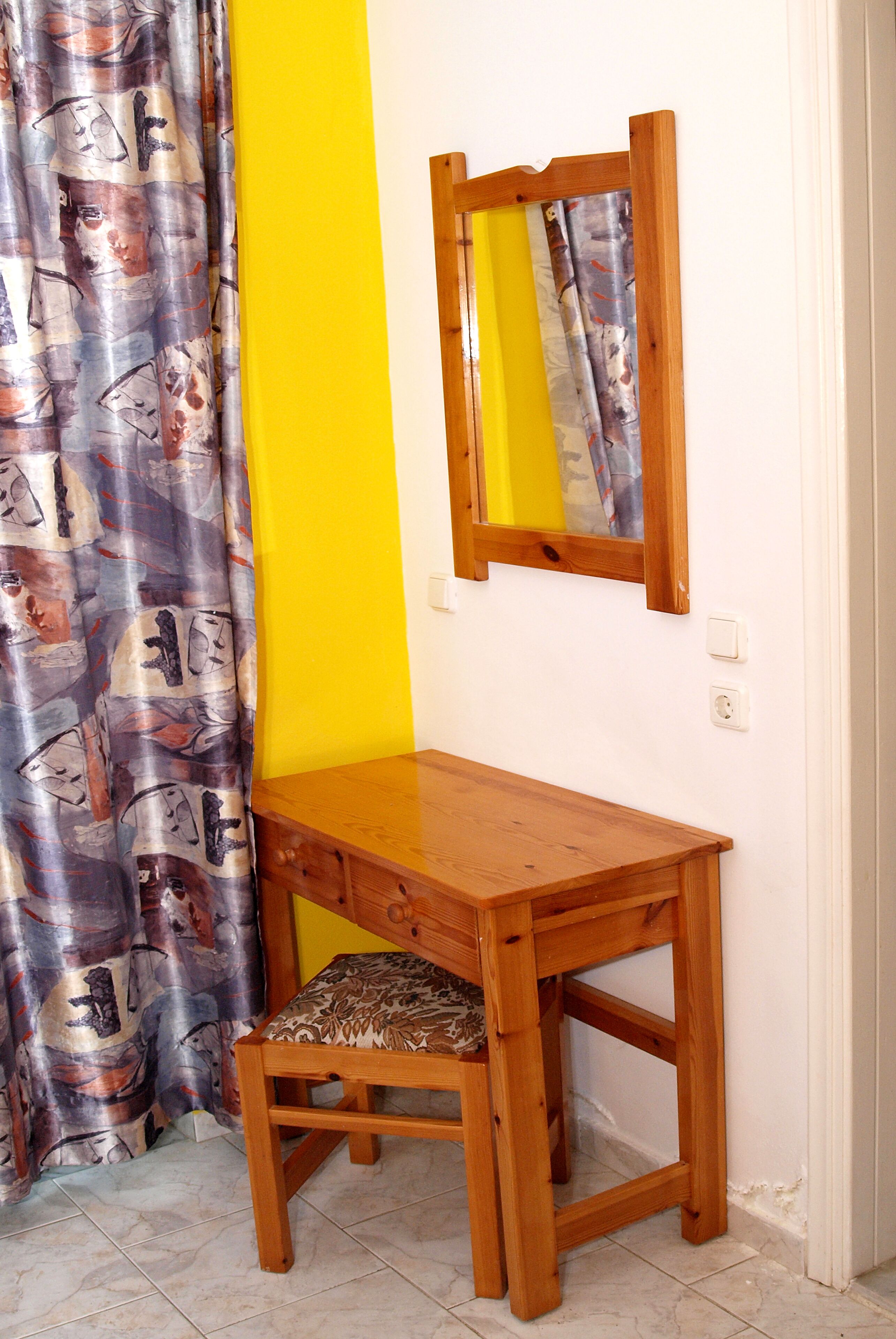 Ein Holztisch mit Stuhl, einem Spiegel und einer gelben Wand.