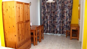 A room with a wooden wardrobe, a dining table with chairs, a small wooden stool, and a curtain with a pattern. - Marianthi Studios Stegna (Rhodes)