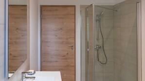 Ein modernes Badezimmer mit einer gläsernen Duschkabine, einem weißen Waschbecken und einer Holztür.