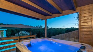 Un bain à remous avec une terrasse en bois et une vue sur un mur de pierres et des arbres.