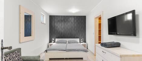 A bedroom with a bed, a dresser, a television, and a window.