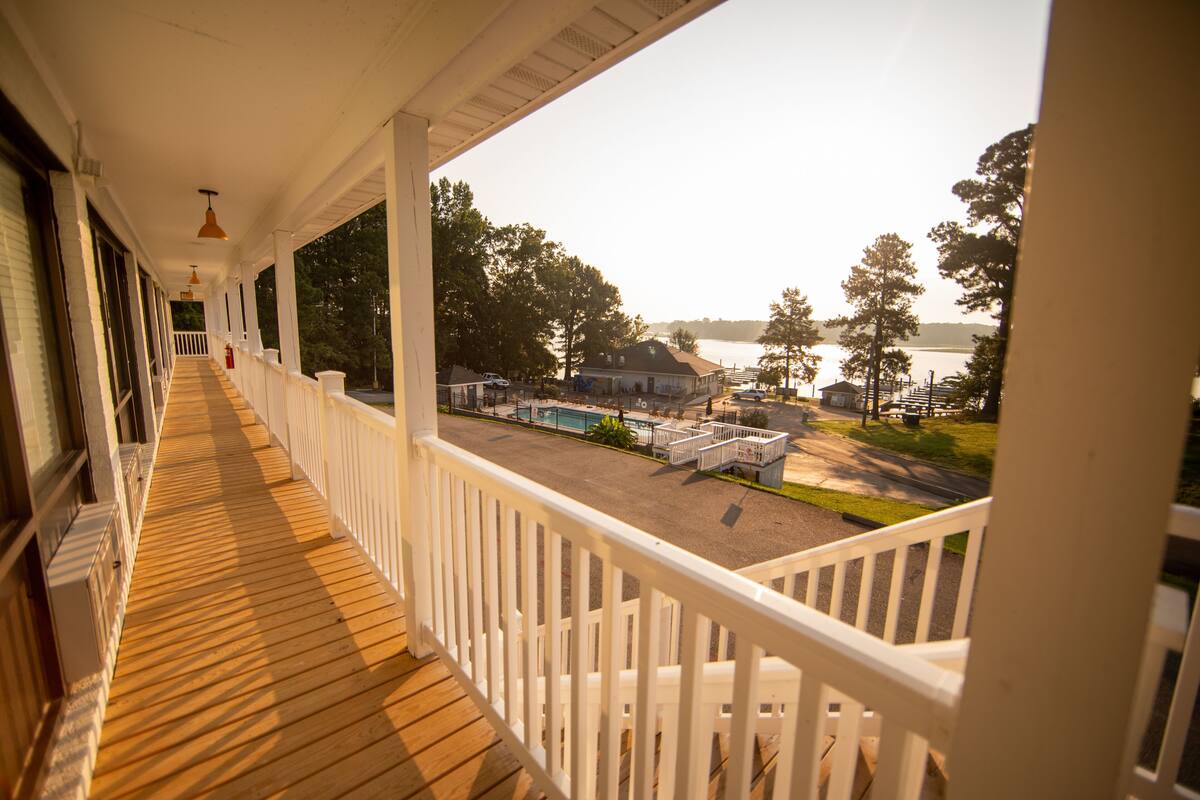 A wooden deck with white railings overlooking a swimming pool and a lake.