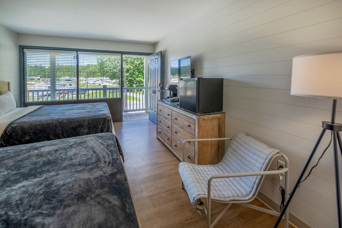 A room with two beds, a desk with a computer, a chair, a TV, and a large window with blinds.