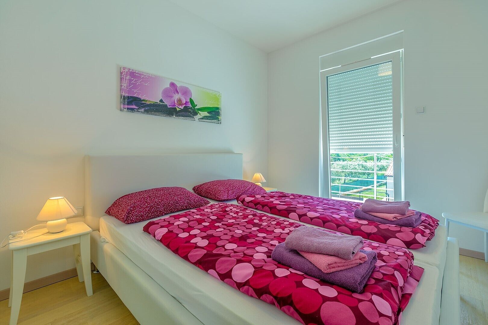 Ein Schlafzimmer mit einem großen Bett, zwei Nachttischen, einem Fenster mit Jalousien und einem Wandbild.