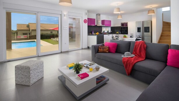 A modern living room with a grey sofa, a coffee table, and a view of a pool through large sliding doors. - Villa Stefanja in Galizana (Galizana)