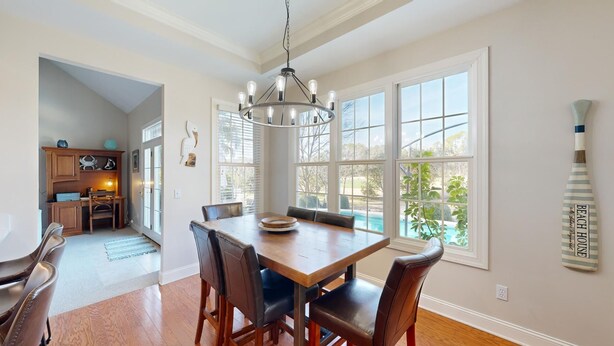 Un comedor con mesa y sillas de madera, ventanas amplias y vista a una piscina.