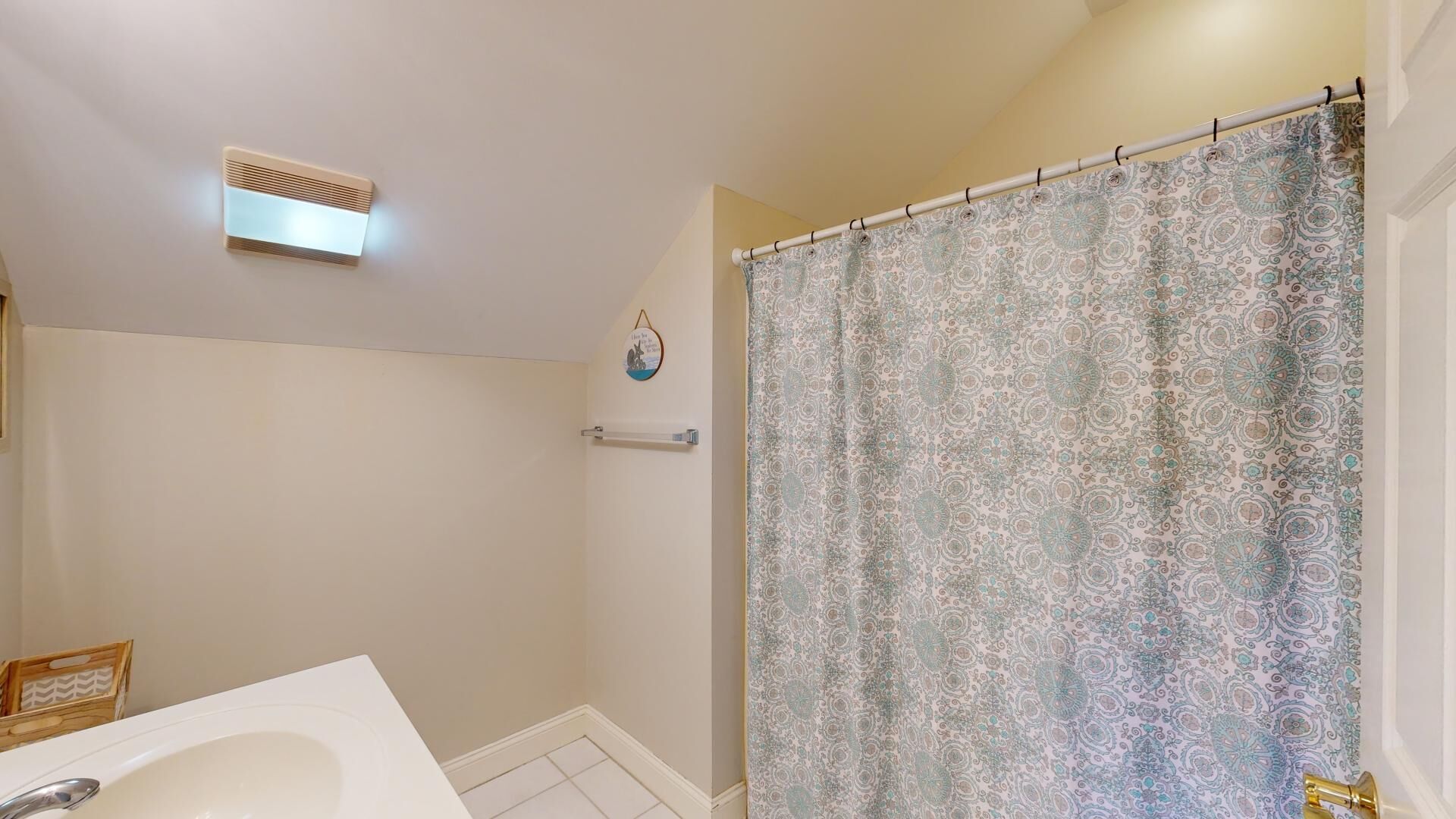 Een badkamer met douchegordijn, handdoekrek en een ventilatierooster aan de muur.