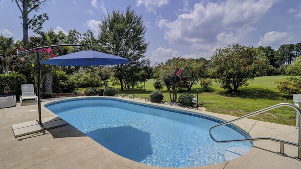 Una piscina con una sombrilla azul, una escalera metálica y una silla de descanso blanca.