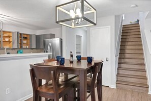 A modern kitchen with a dining table and chairs, a built-in oven, and a refrigerator.