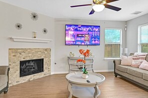 A living room with a fireplace, a television mounted on the wall, a ceiling fan, and a sofa with cushions.