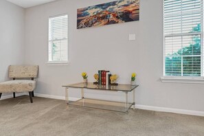 A room with a glass-top table, a chair, and a painting on the wall.