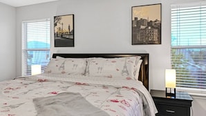 Une chambre à coucher avec un lit, deux tables de chevet et une fenêtre avec des stores.