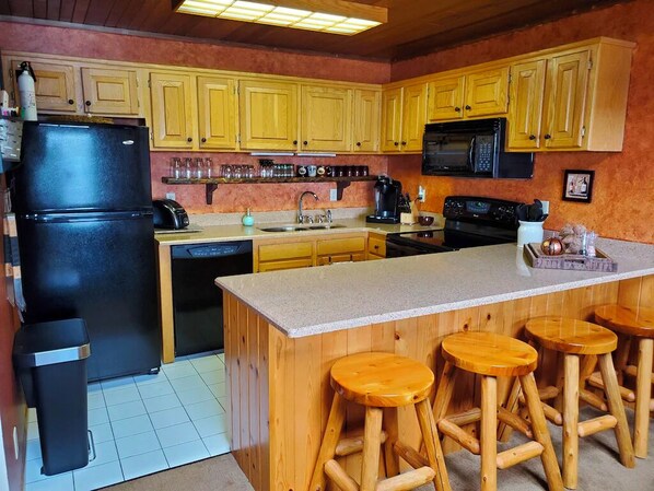 A kitchen with wooden cabinets, a black refrigerator, a microwave, a stove, and wooden stools at the island.