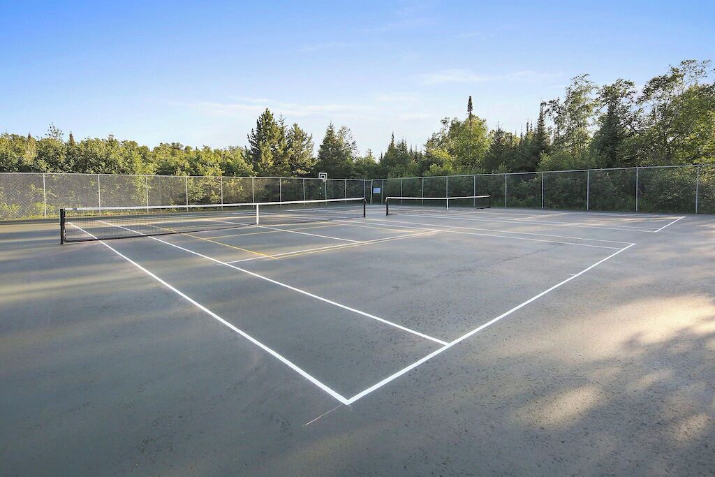 Een buitenbaan voor tennis met een net, omringd door bomen en een heldere lucht.