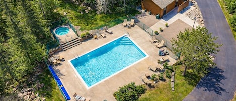 Une piscine rectangulaire avec un petit jacuzzi, entourée de chaises longues et d’une terrasse en bois.