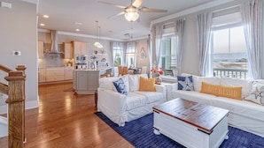 A spacious living room with a large window, a ceiling fan, and a view of the beach. - Starfish Waterfront Family Retreat, Steps to Sound (Navarre)