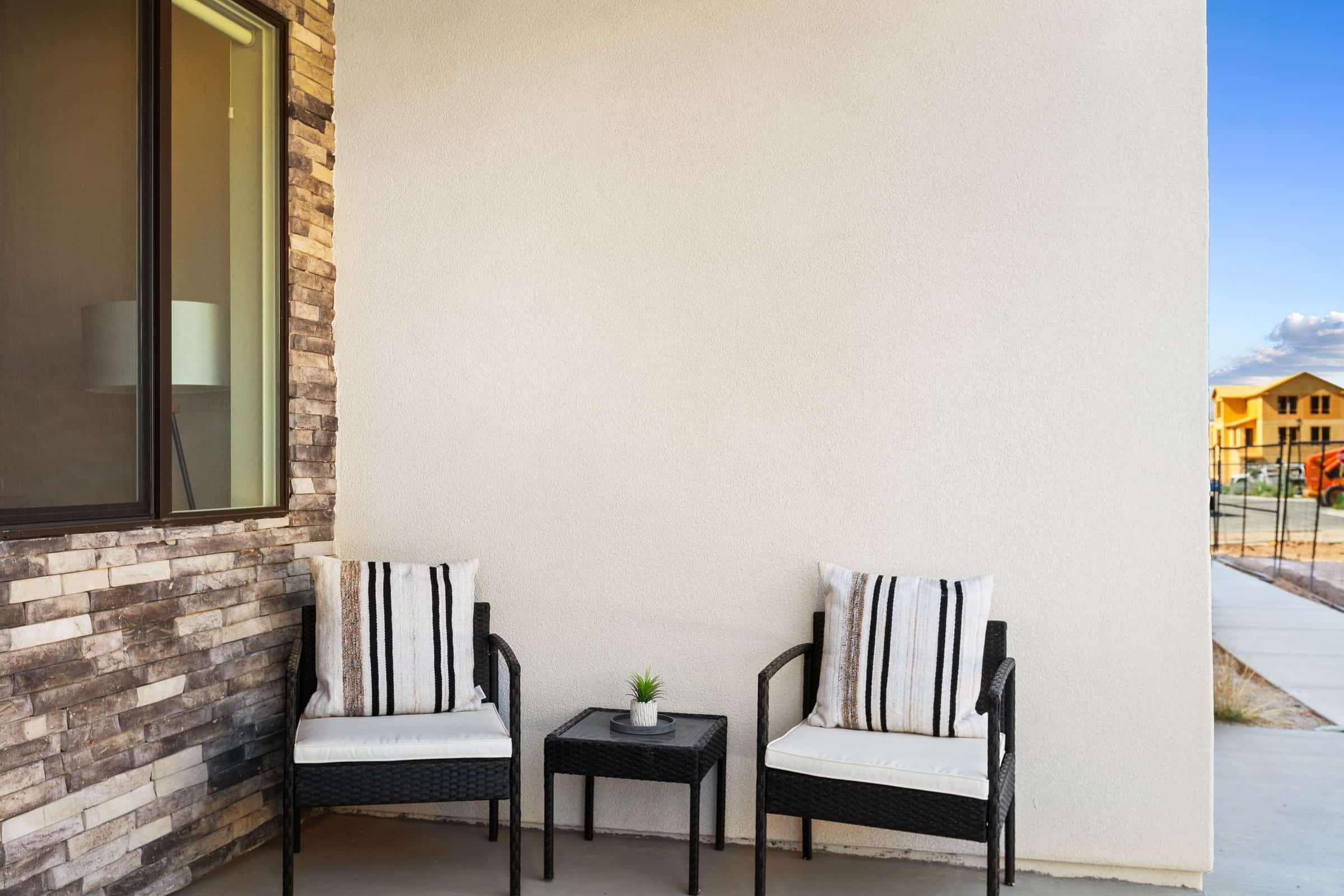 Zwei Korbstühle mit gestreifter Polsterung auf einem Balkon mit einem kleinen Tisch und einem Blumentopf.
