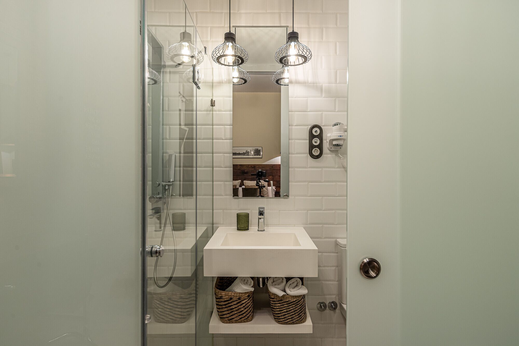 A bathroom with a glass shower enclosure, a white sink, and a mirror above it.