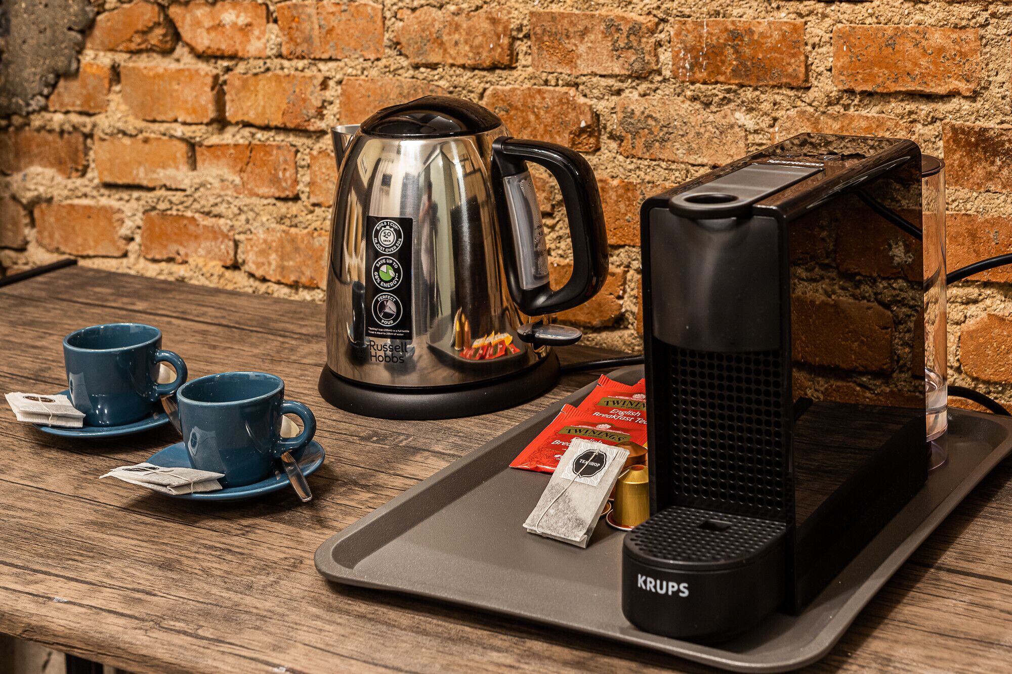 Een koffiehoek met een waterkoker, koffiezetapparaat en kopjes op een dienblad.