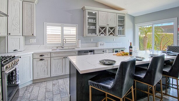 A modern kitchen with white cabinetry, a large island, and a dining area with black leather chairs. - Pool and Spa + Close to Disney +Game Room (Anaheim)