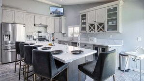 A modern kitchen with a central island, stainless steel appliances, and a flat-screen TV mounted above the island. - Pool and Spa + Close to Disney +Game Room (Anaheim)