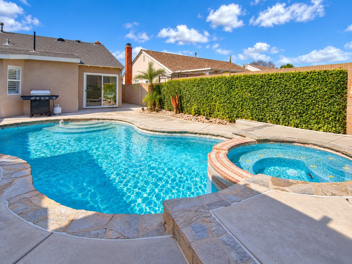 A backyard with a swimming pool, a barbecue grill, and a house.
