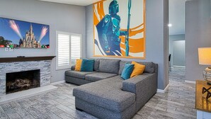 A living room with a fireplace, grey sofa, and a large wall mural. - Pool and Spa + Close to Disney +Game Room (Anaheim)