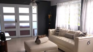 A living room with a white sofa, an ottoman, a ceiling fan, and a door with frosted glass panels. - Exclusive and spacious house in Guaynabo (Guaynabo)