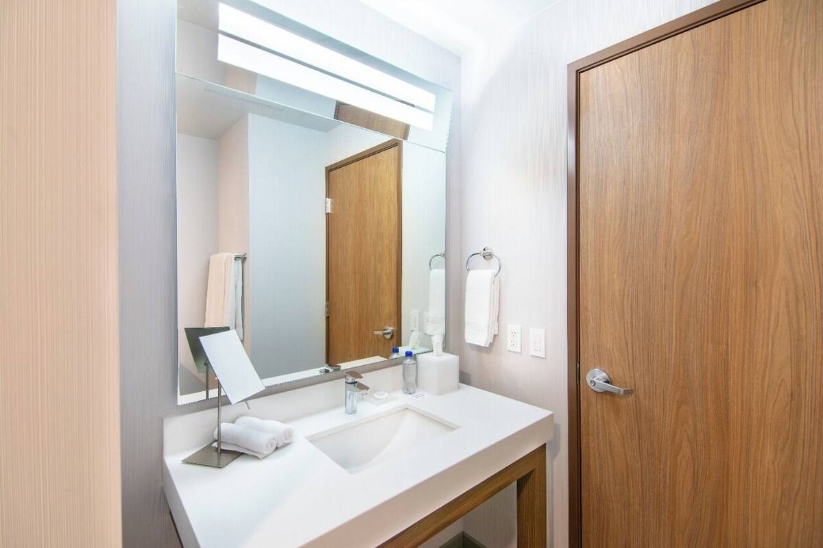 A modern bathroom with a white sink, a large mirror, and a wooden door.