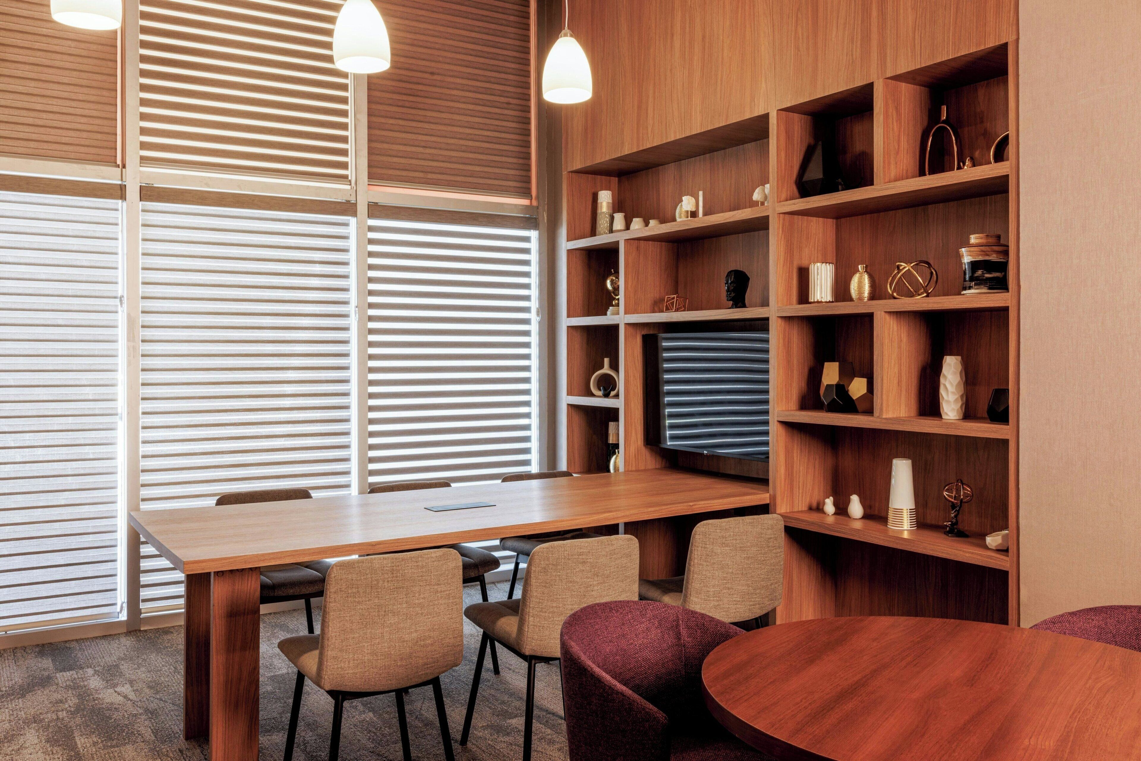 A modern meeting room with a wooden table, chairs, and a bookshelf with decorative items.