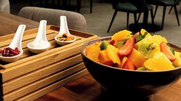 Una mesa de madera con un bol de fruta variada y tres cucharas blancas con diferentes alimentos.