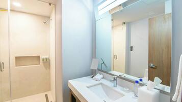 A modern bathroom with a glass-enclosed shower, a large mirror, and a white sink with toiletries.