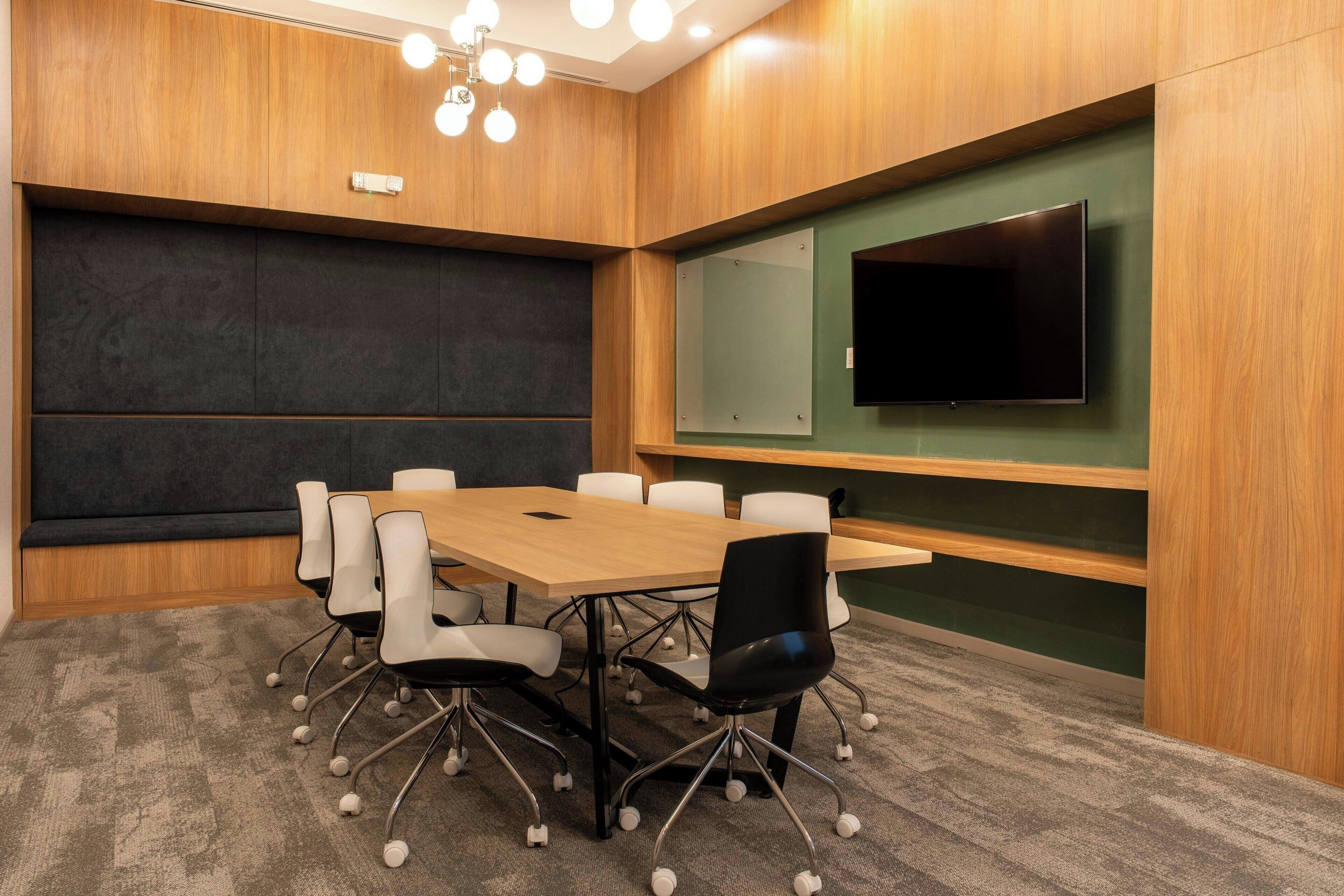 A conference room with a wooden table, white and black chairs, a large screen, and a green accent wall.