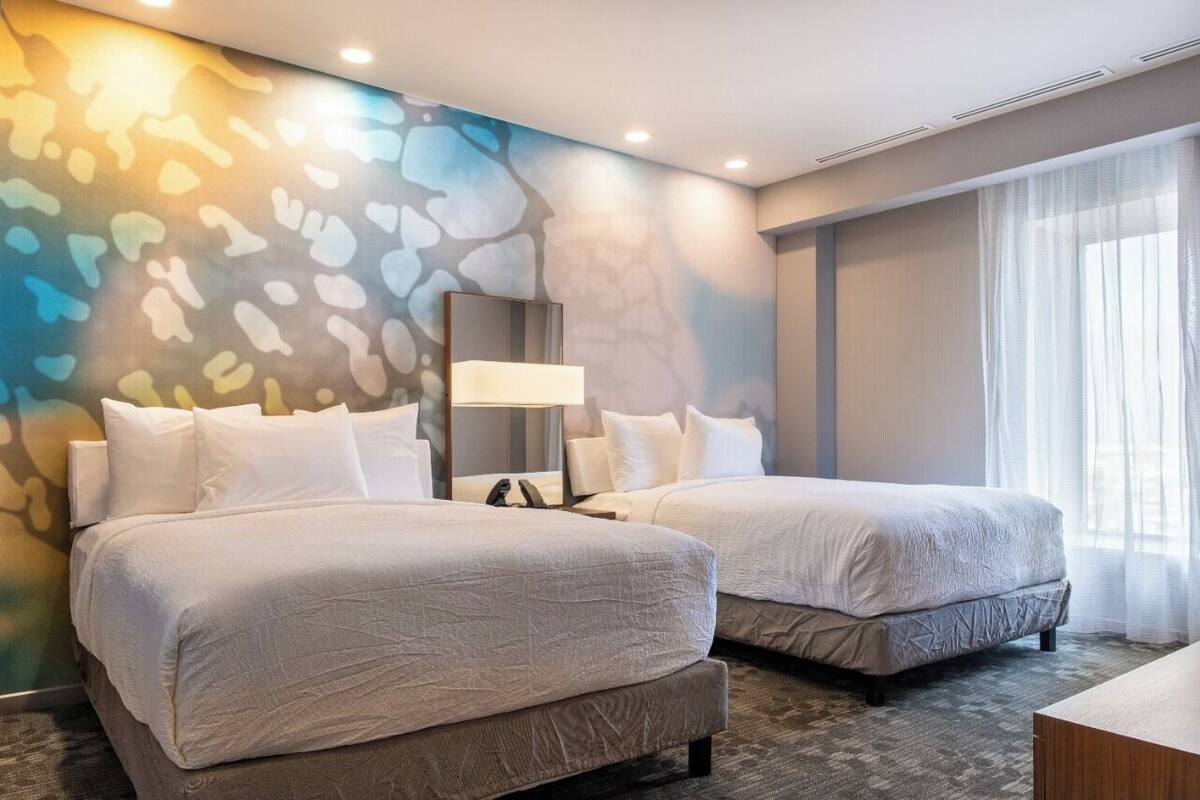 A hotel room with two beds, a large mirror, and a wall with a colorful abstract design.