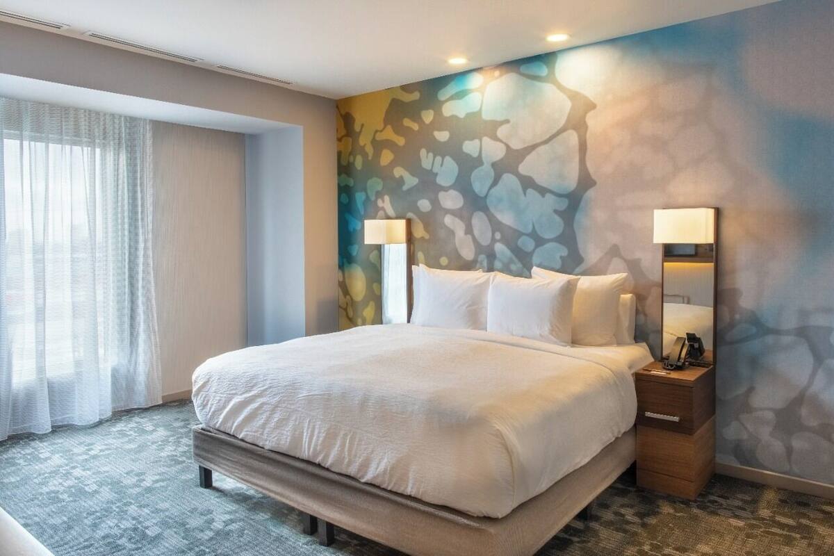 A hotel room with a large bed, two bedside tables, a nightstand, a mirror, and a wall mural.