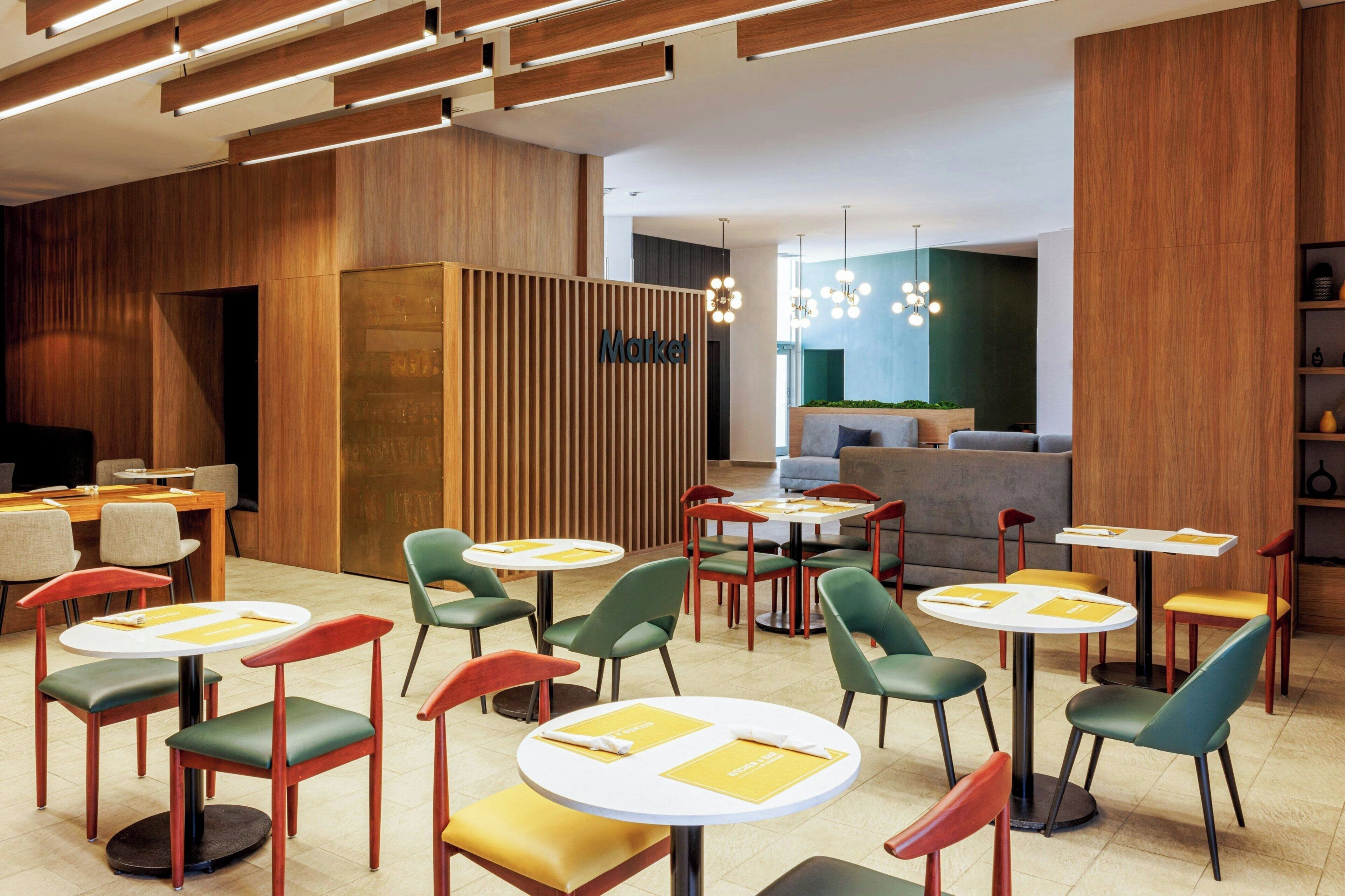 Interior de un restaurante moderno con mesas y sillas redondas, un mostrador de recepción de madera y una zona de estar con sofá.