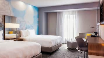 Habitación de hotel con dos camas, un escritorio, una silla, un espejo grande y una ventana con cortinas.