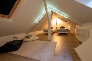 Una camera da letto mansardata accogliente, con soffitto spiovente, un letto con cuscini, un piccolo tappeto e luci a stringa.