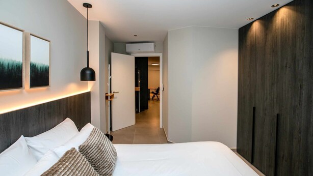 A modern hotel room with a large bed, a wardrobe, a bedside table, and a hallway leading to a bathroom. - Mocho-rural -home Adaptado (Beceite)