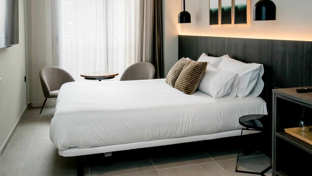 Une chambre d’hôtel moderne avec un grand lit, deux fauteuils, une petite table et des œuvres d’art accrochées au mur.