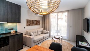 A modern living room with a sofa, a dining table, and a kitchen area with dark cabinets and a tiled backsplash. - Mocho-rural-home Lonja B (Beceite)